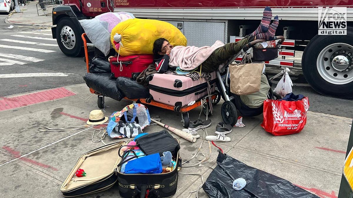 A man asleep on a street surrounded by trash and clothes