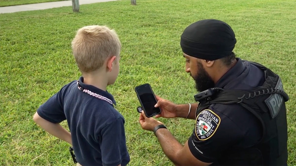 Child and officer examine coin with QR code using smartphone