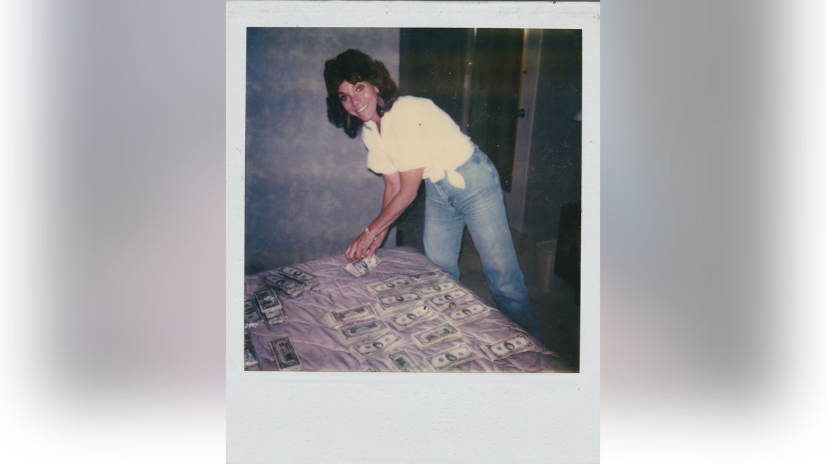 A woman smiling in a white shirt and blue jeans in front of a lot of money