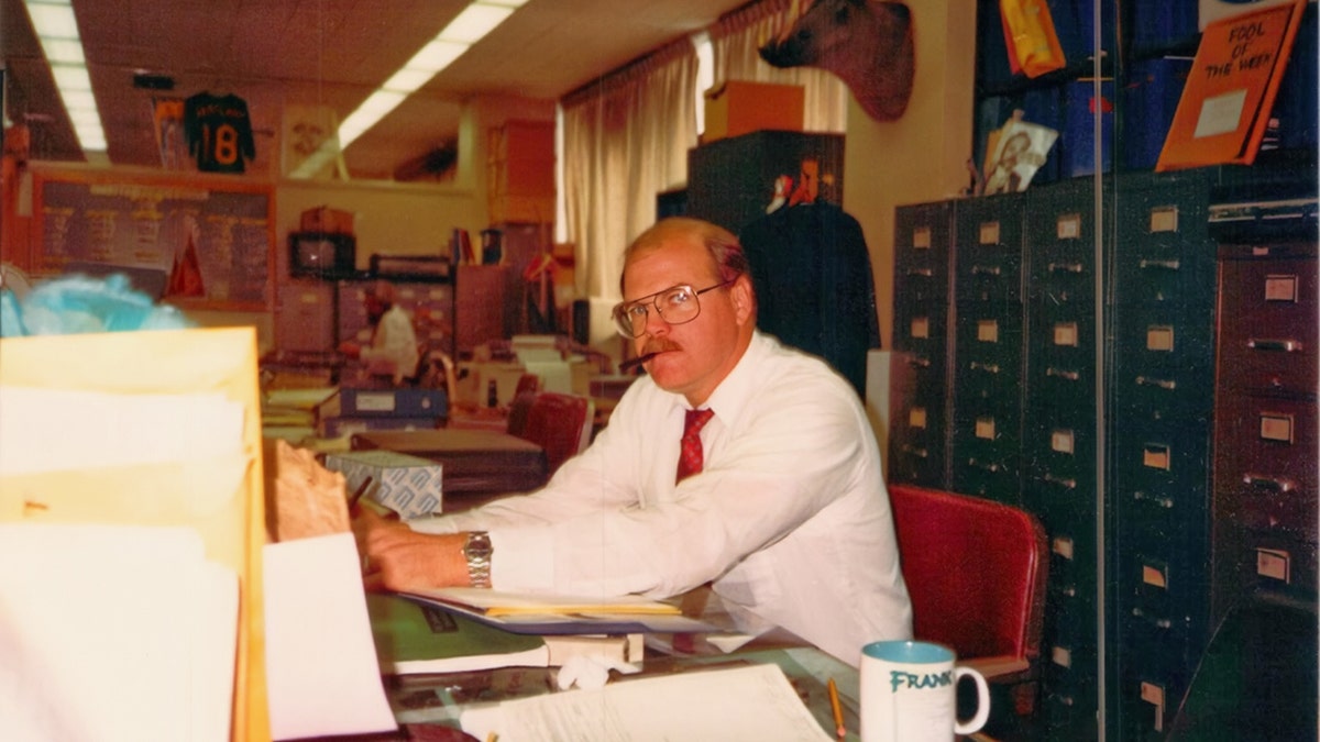 Rick Jackson in a white shirt and red tie sitting at a desk.