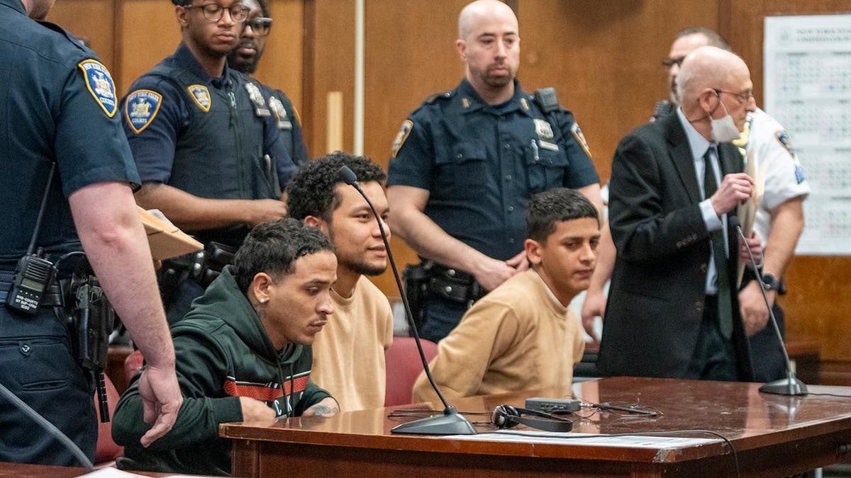 Three migrants sit at a desk in court