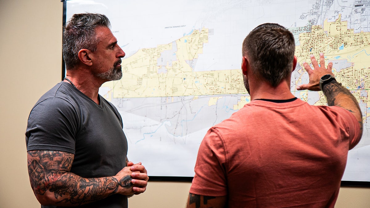 Lou Valoze looking at a map and speaking to an officer in regular clothing.