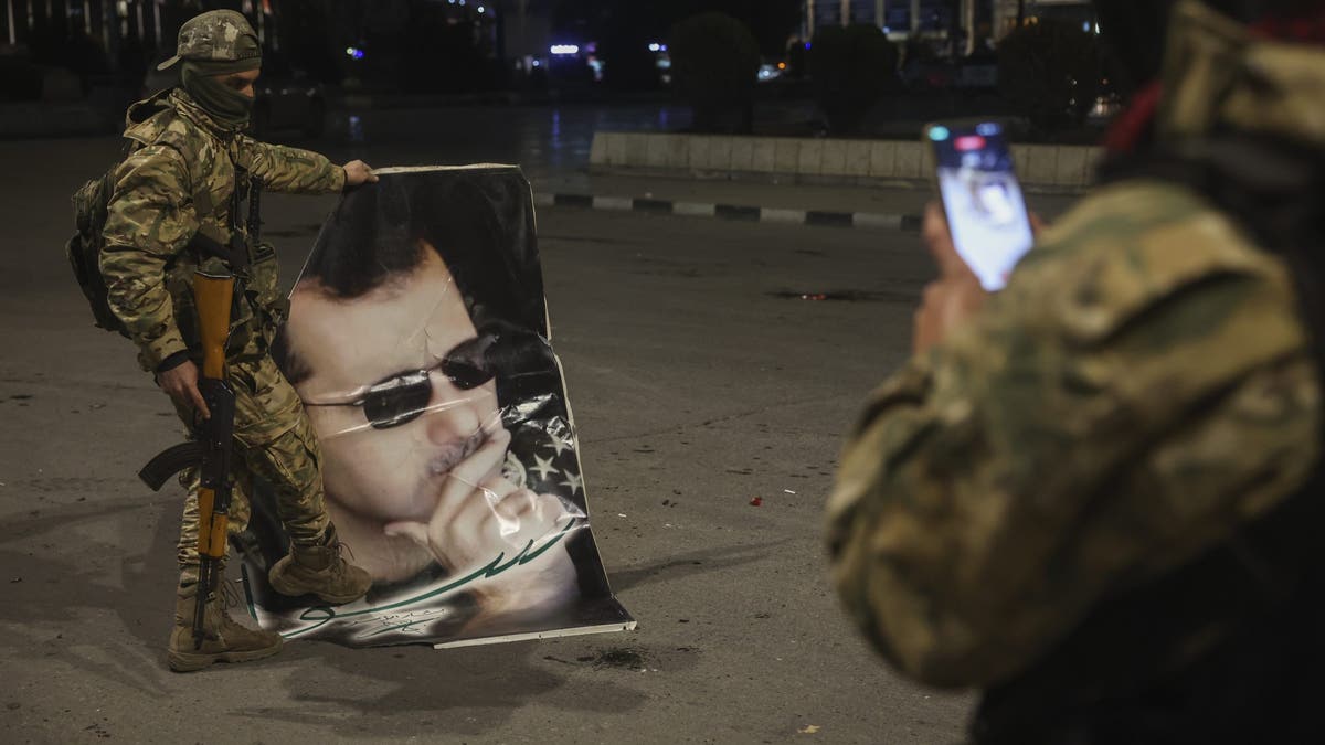 A Syrian opposition fighter takes a picture of a comrade stepping on a portrait of Syrian President Bashar Assad in Aleppo, early on Saturday Nov. 30, 2024. (AP Photo/Ghaith Alsayed)