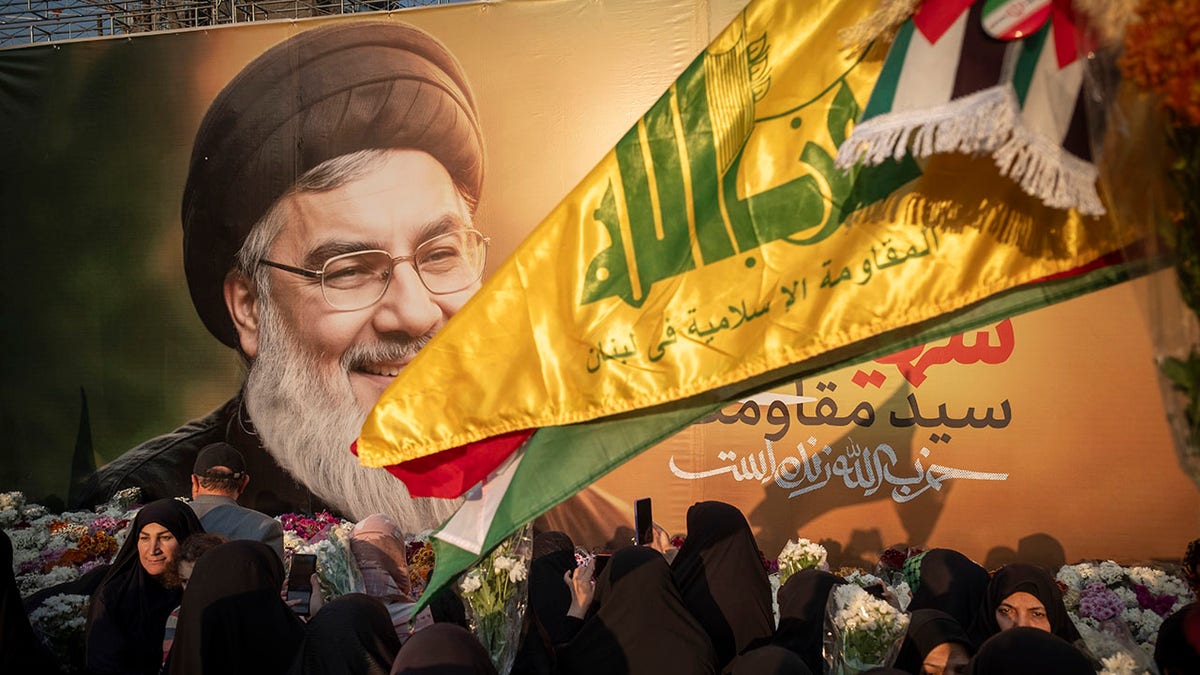 Iranian protesters carry flowers while standing in front of a giant banner depicting a portrait of Lebanon's Hezbollah Secretary General Hassan Nasrallah during a protest gathering to condemn an Israeli air strike against Hezbollah's headquarters in the suburb of Beirut and the killing of Hassan Nasrallah and an Islamic Revolutionary Guard Corps' Quds Force commander, General Abbas Nilforoushan, in Tehran, Iran, on Sept. 30, 2024.