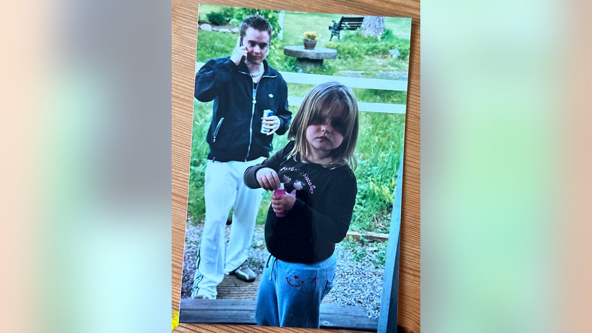 A young Jamie-Lee Arrow standing in front of her father Isakin Jonsson outdoors.