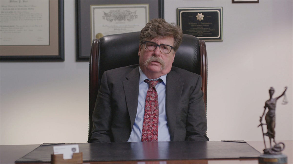 Bill Portanova wearing a suit and sitting on a leather chair.