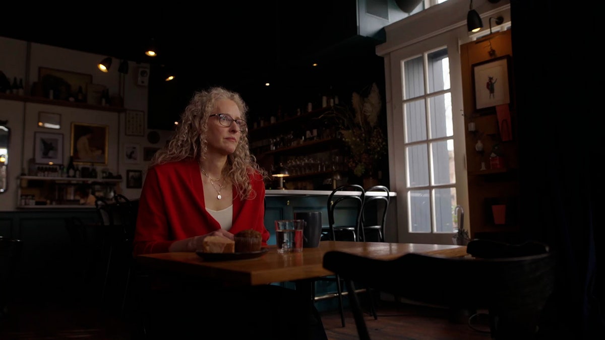 Denise Farmer wearing a red blazer and a beige blouse with glasses.