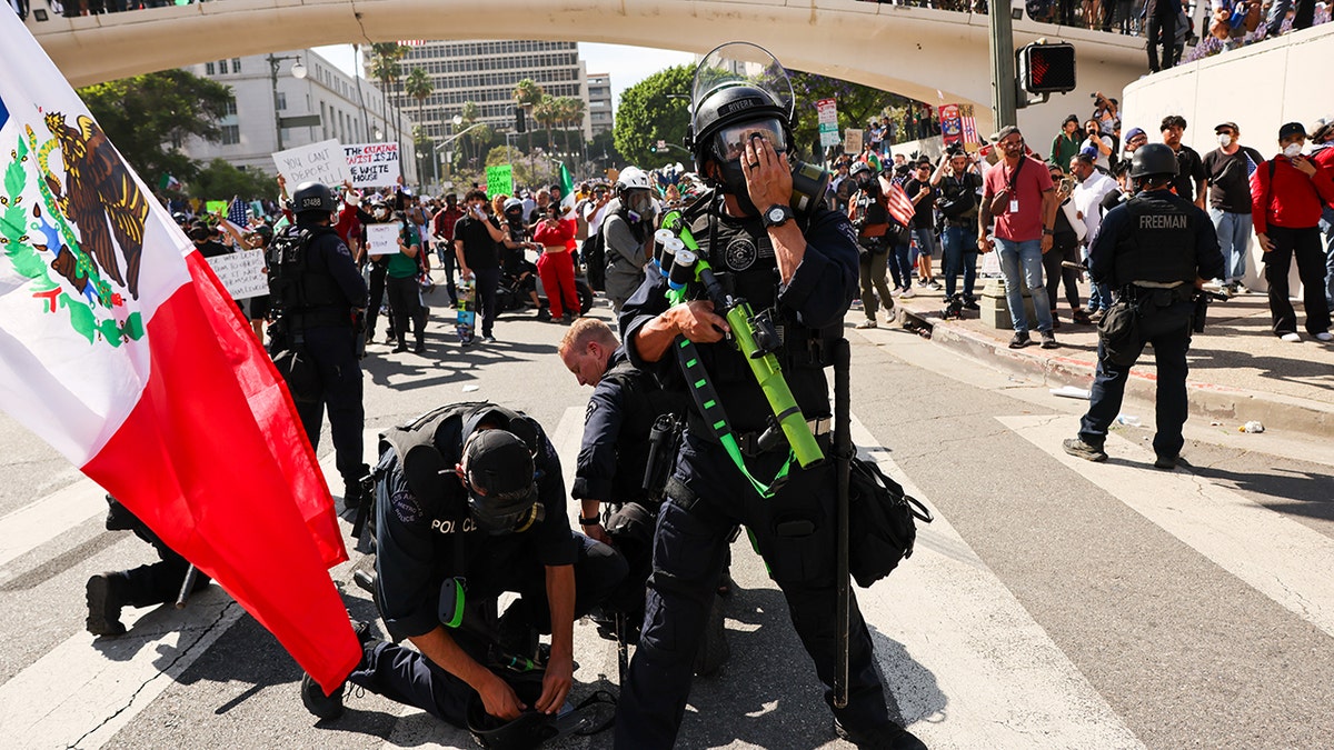 cops arresting protester in street; mexican flag at left in frame