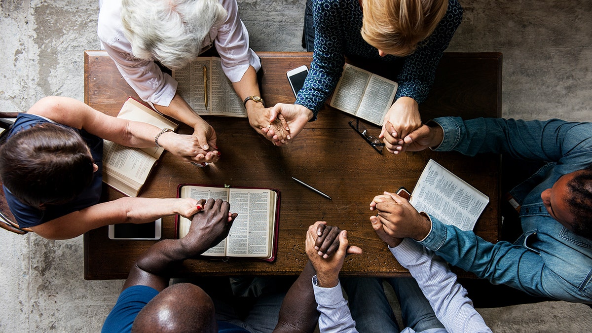 A diverse group joins hands in prayer during a Bible study
