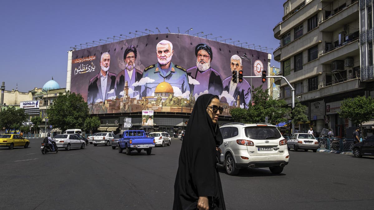 People move past a large banner featuring portraits of slain leaders from Iran-aligned armed groups, including Hamas leader Yahya Sinwar, Hezbollah leader Hassan Nasrallah and Iranian Commander Qasem Soleimani, in central Tehran, Iran, on May 1, 2025.