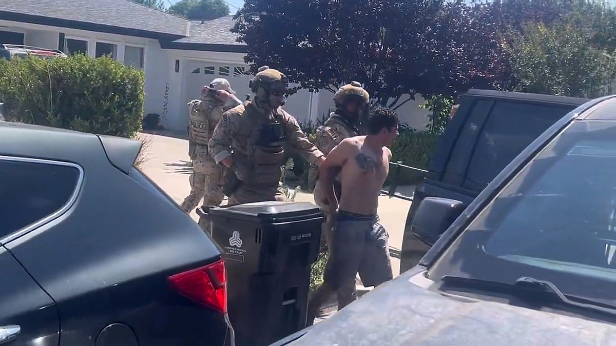 federal officials escort shirtless suspect from house to vehicle