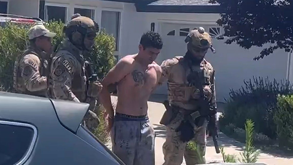 federal officials escort shirtless suspect from house to vehicle