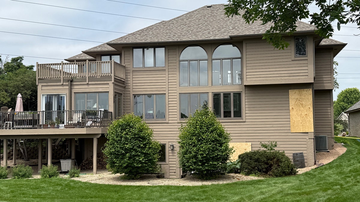 rear side of large beige house with some windows boarded up