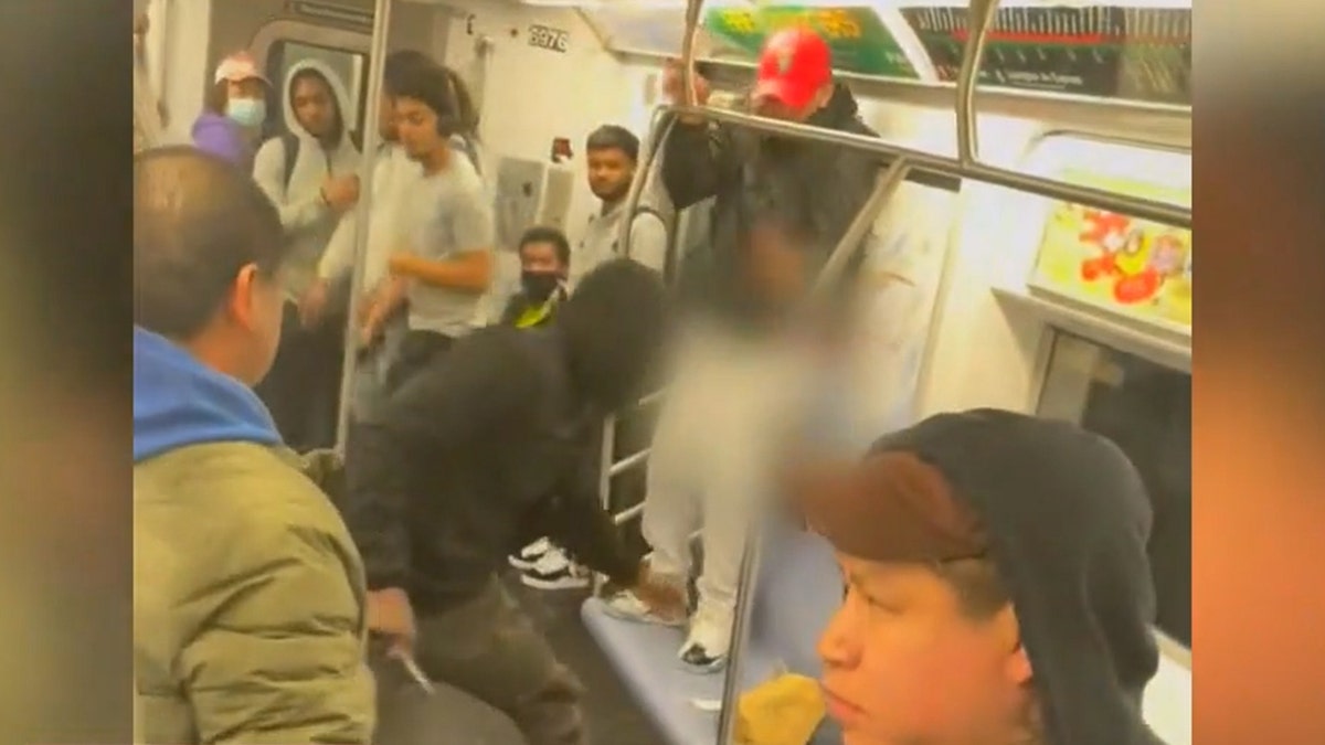 man in black hoodie weilding knife as he corners another man in train car