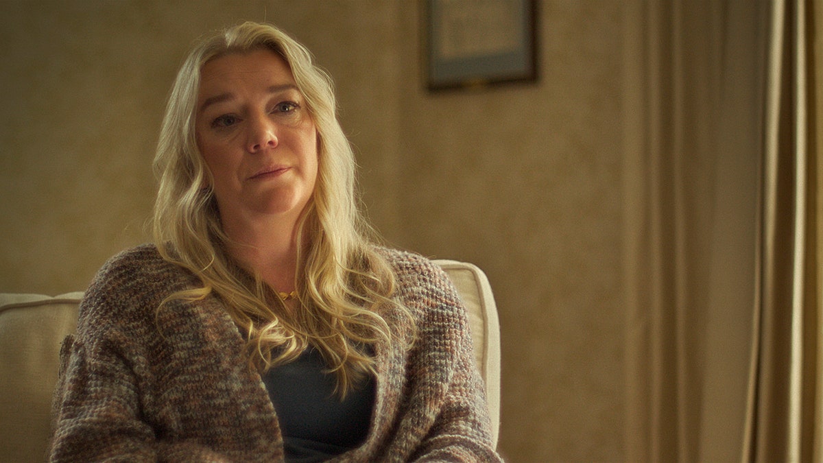 Karen Laramie sitting down wearing a grey sweater looking somber.