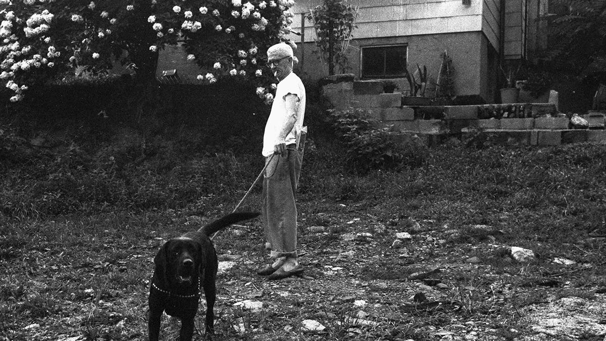 A black and white photo of a man walking his black dog.