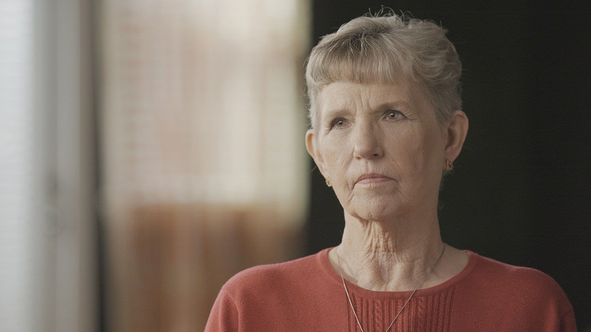 Debbie Stellas wearing a coral sweater and a thin gold necklace.