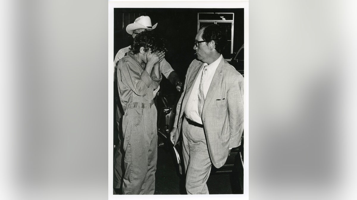 Elmer Wayne Henley Jr. covering his face while being arrested.
