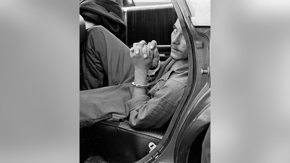 Elmer Wayne Henley Jr. holding his hands inside a car while handcuffed.