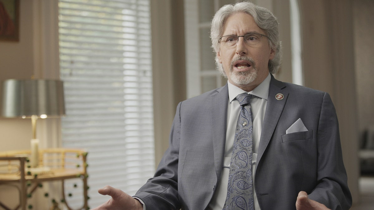 Jerome Elam wears a grey suit and is in mid-sentence speaking.