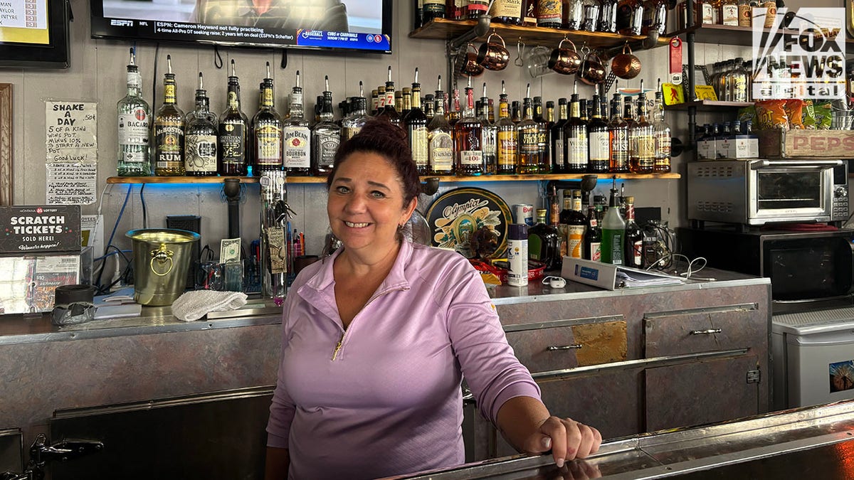 Bartender Jill Rowles behind bar in in front of liquor bottles wearing purple shirt
