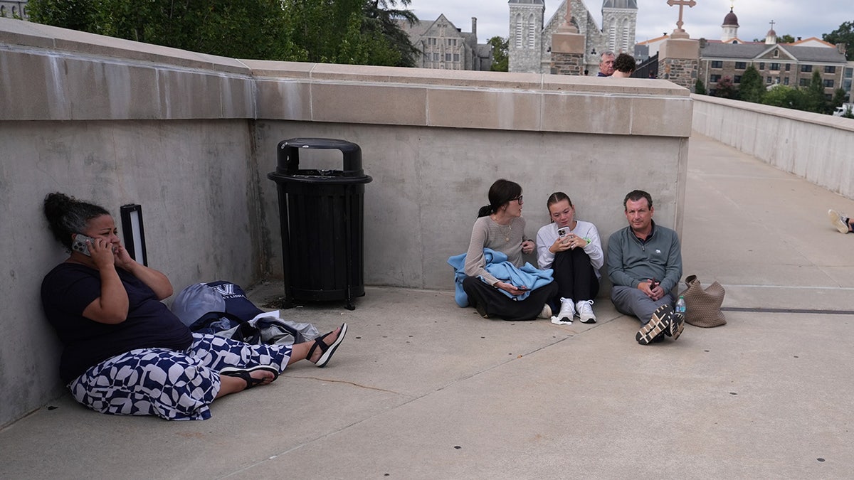 People shelter behind a wall on the Villanova University campus in Villanova, Pa., on Thursday, Aug. 21, 2025, where an active shooter was reported.
