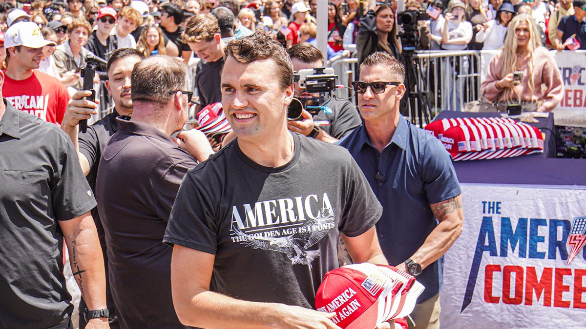 Charlie Kirk smiling while throwing MAGA hats