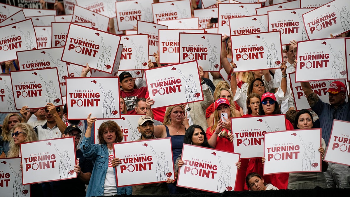 People hold up signs at Kirk memorial
