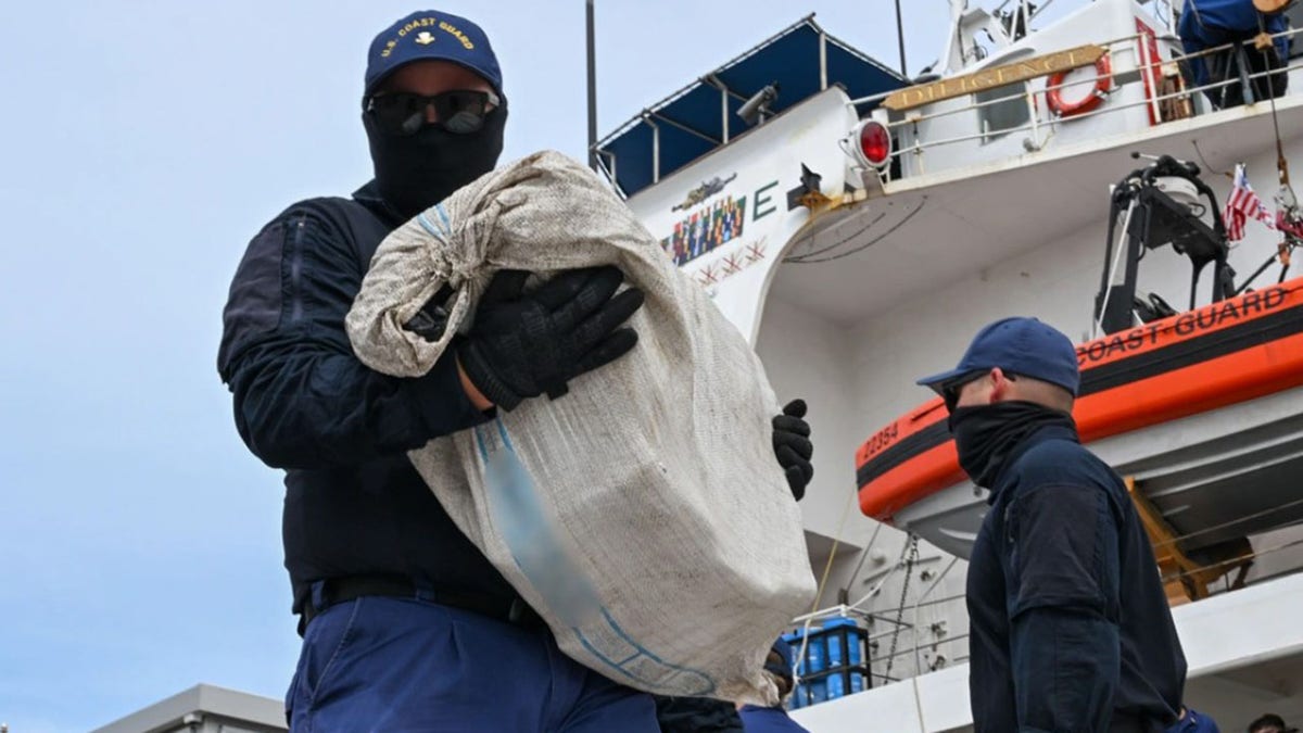 A member of the Coast Guard carries a bag filed with illegal drugs