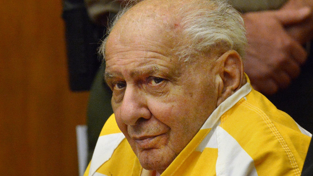 Joseph Naso smirking wearing a yellow and white inmate shirt in court.