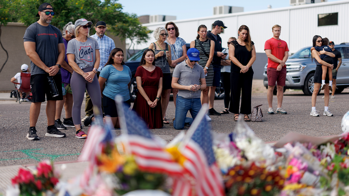 A group of people pray outside a makeshift memorial for Charlie Kirk, which consists of flowers and American flags