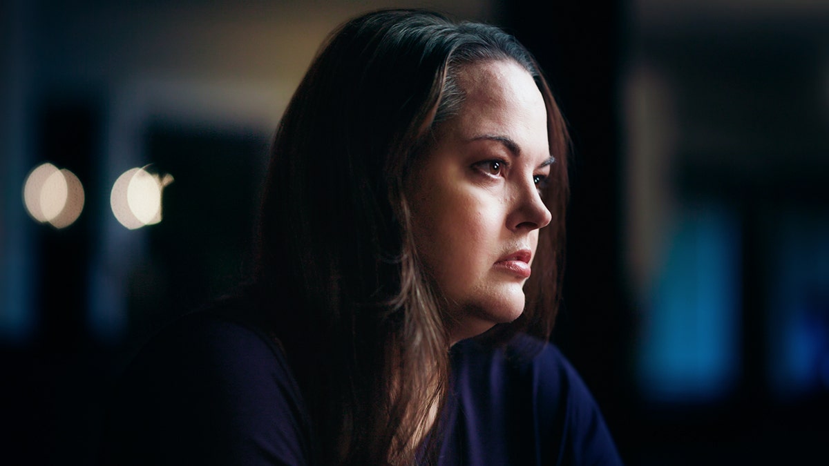 A side profile of Kerri Rawson looking pensive in a dark room.