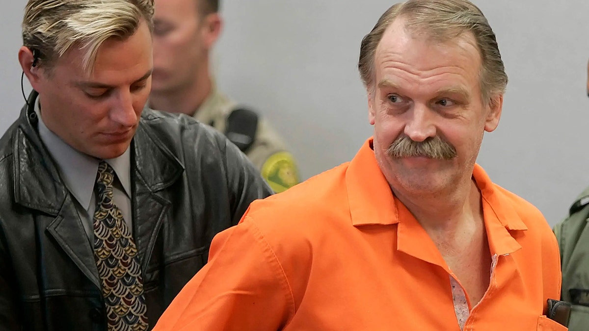 Ron Lafferty being handcuffed as he smirks in an orange jumpsuit.