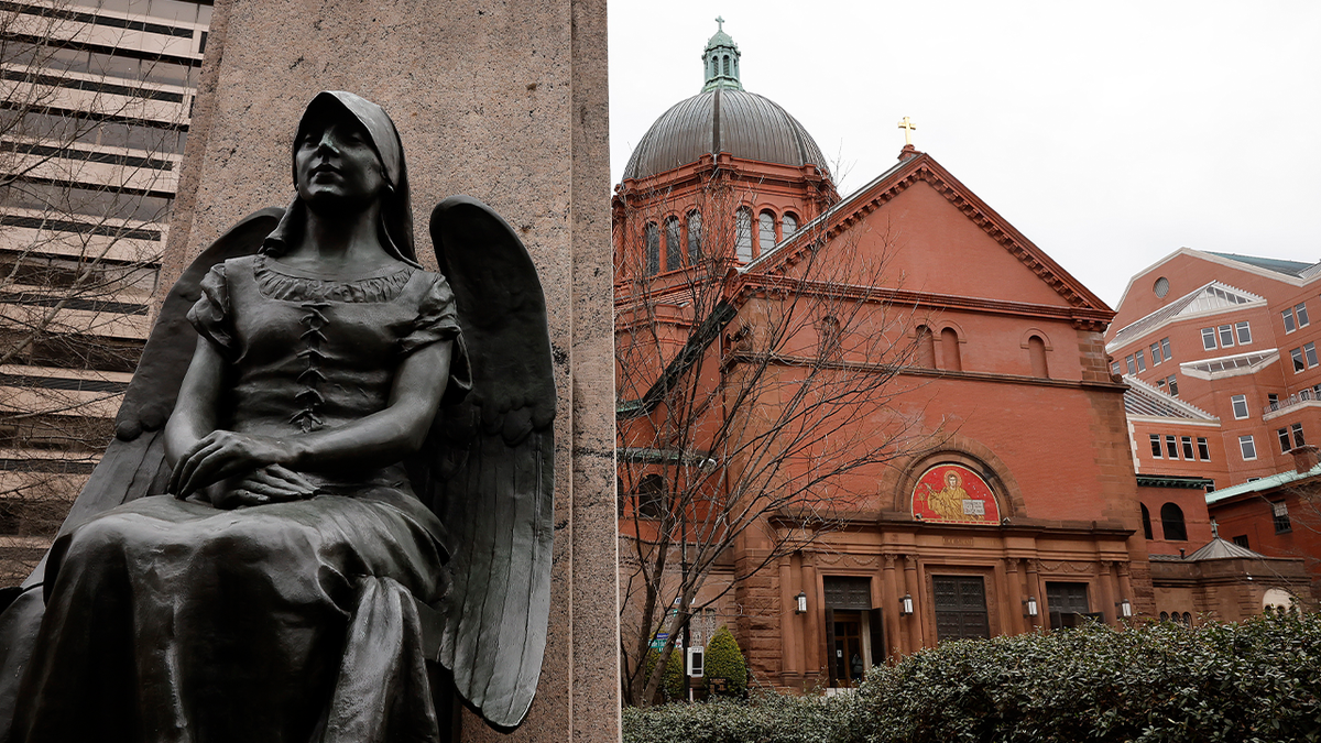 A religious statue in the foreground in front of the red brick walls of The Roman Catholic Cathedral of St. Matthew the Apostle