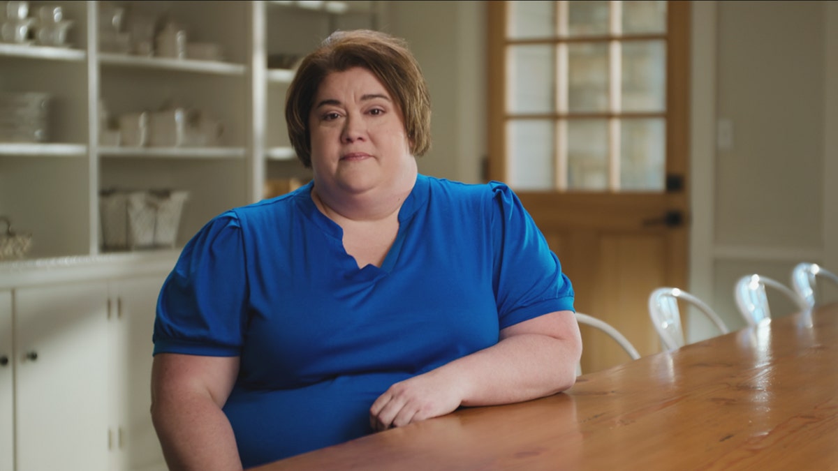 Stacey Rutherford looking serious sitting at a table wearing a cobalt blue blouse.