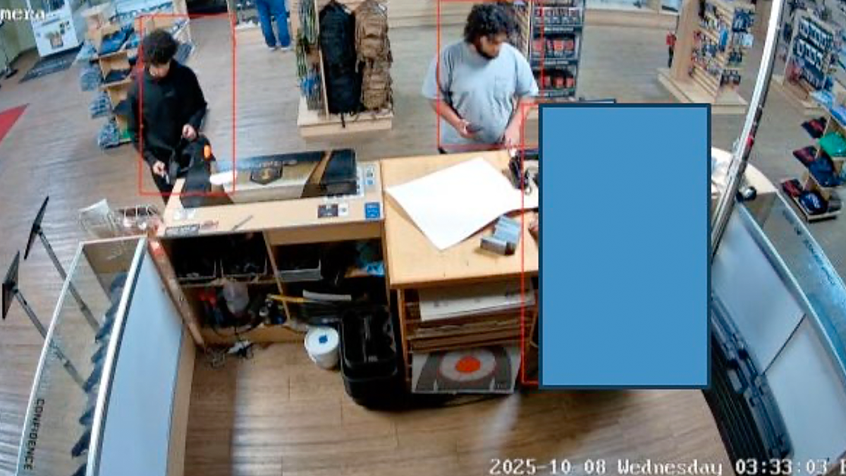 Two men, wearing black and gray shirts, seen in surveillance video at the counter at a gun range.