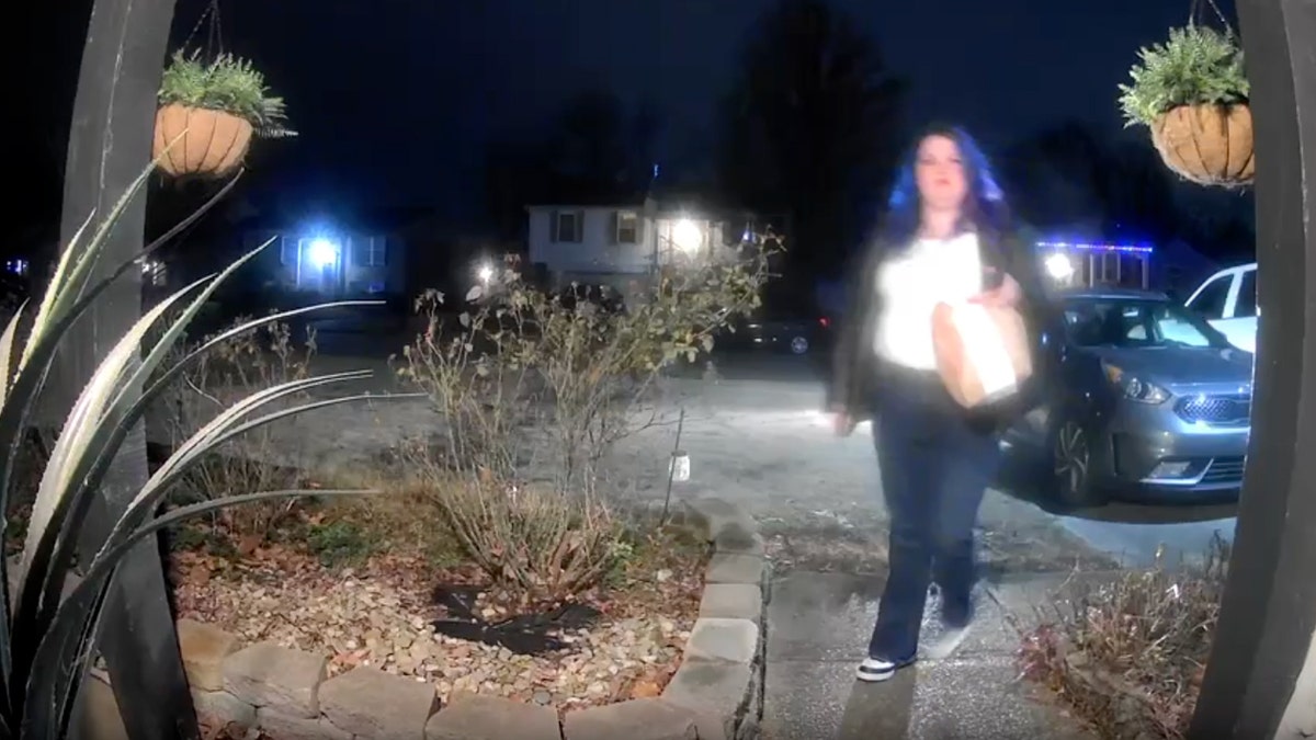 Woman walking in front of house with food order at night.