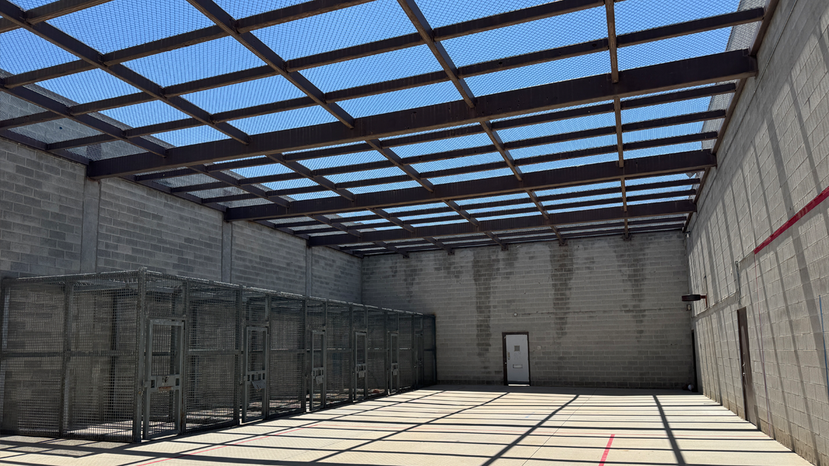 the empty rec yard at Idaho's maximum security prison shows a row of cages on the left and steel bars covering the top section, with the sky showing through a metal mesh