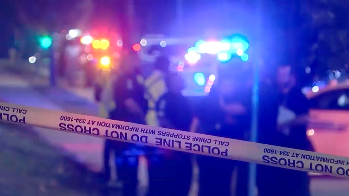 Police line tape stretches across a Charlotte street as officers stand near flashing patrol car lights at night.