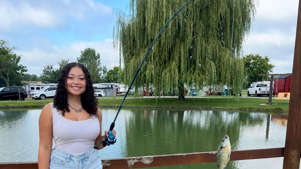 Hailey Buzbee at a lake with a fish at the end of the fishing rod.