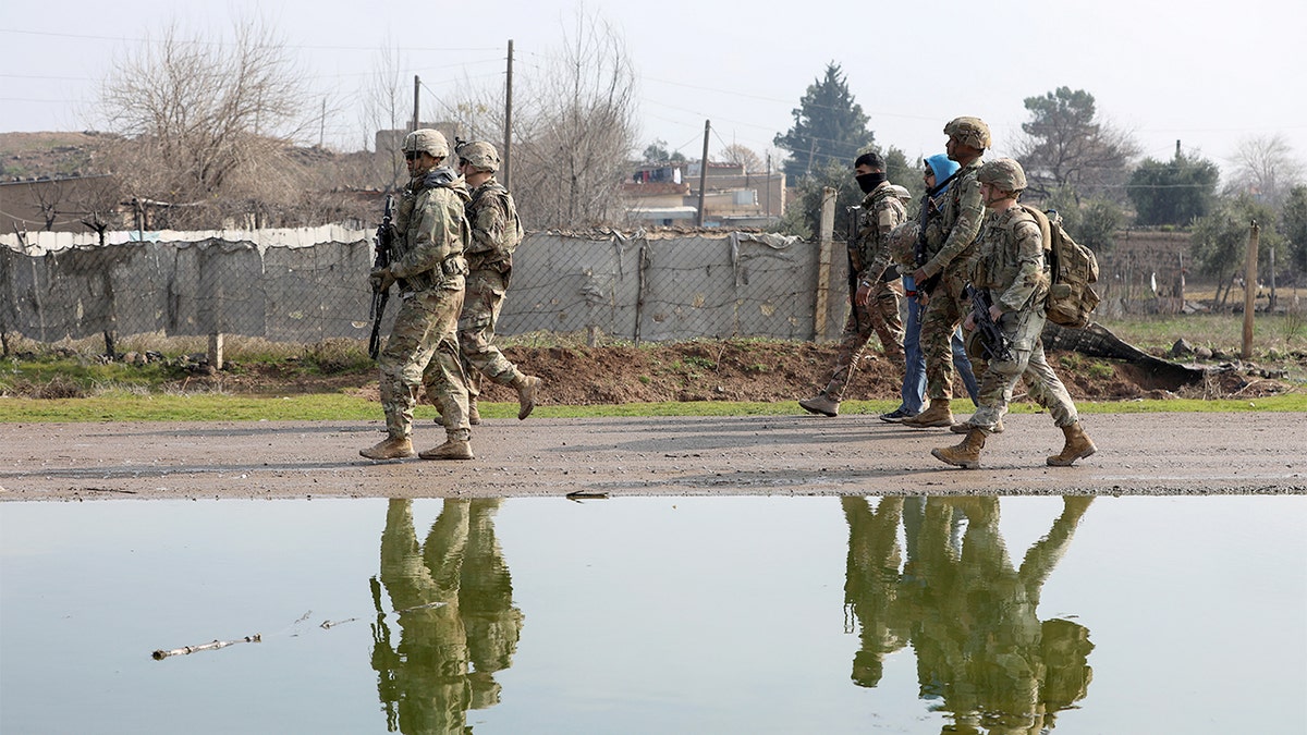 Armed personnel from an international coalition and Kurdish-led forces patrol together along a rural road in northeastern Syria.