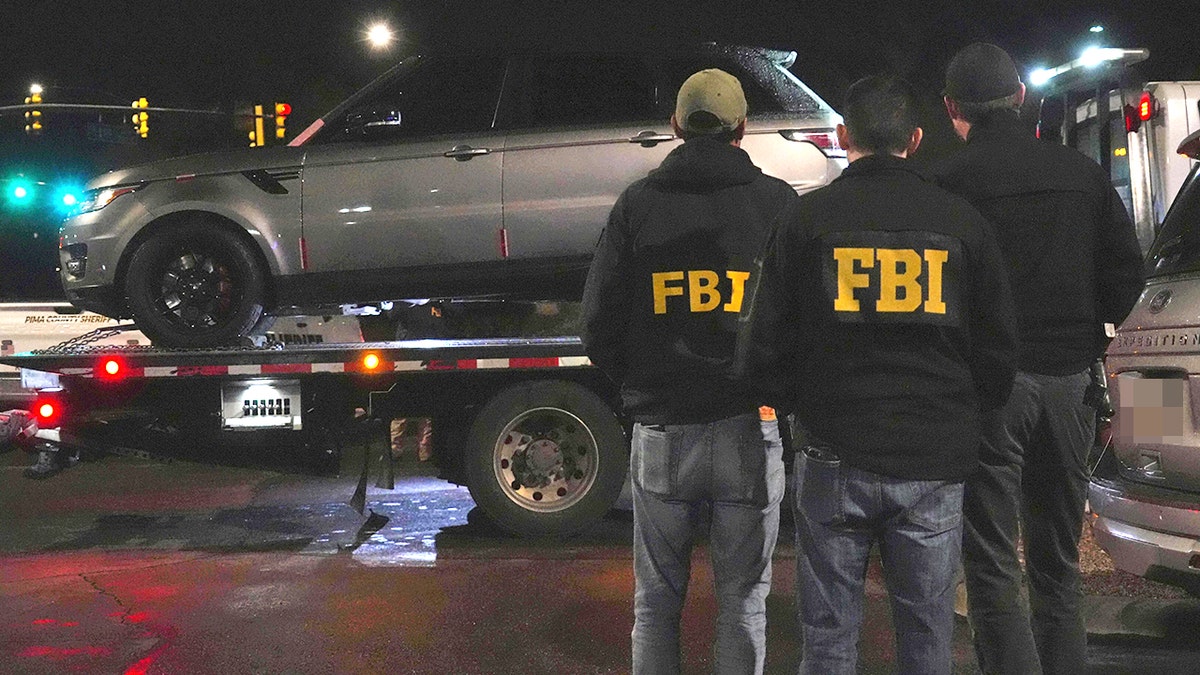 FBI agents and Pima County Sheriff’s deputies, working the Nancy Guthrie case, processing evidence from a gray Range Rover in a parking lot.
